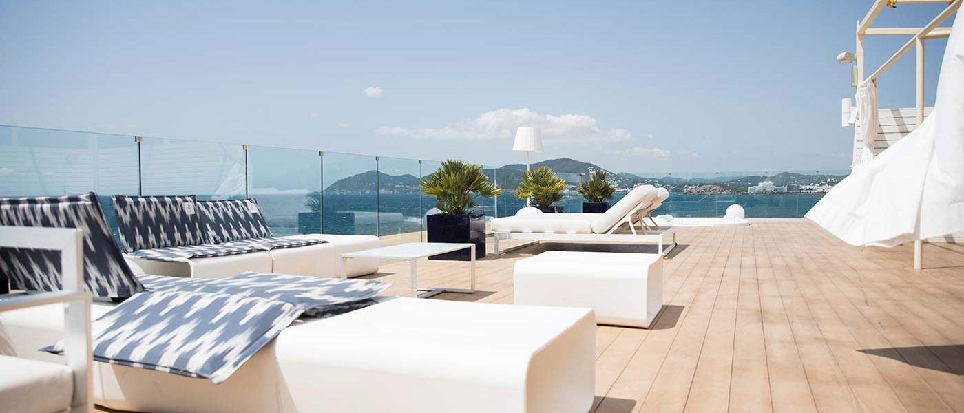 a-roof-top-deck-area-with-white-bright-lounge-chairs-and-spa-overlooking-the-blue-ocean-on-a-sunny_t20_ro7Ydd